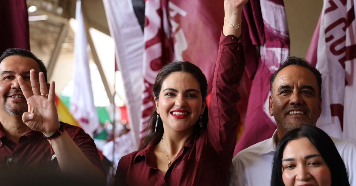 Mujer levanta el brazo durante un acto político con banderas de Morena al fondo