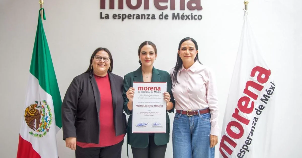 Tres mujeres posan frente a los emblemas de Morena y las banderas de México y del partido; la mujer del centro sostiene un documento