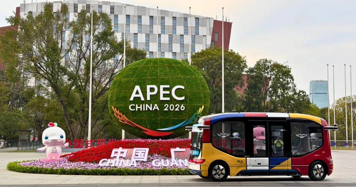 Instalación urbana con el letrero APEC China 2026, flores y un vehículo autónomo frente a edificios y árboles