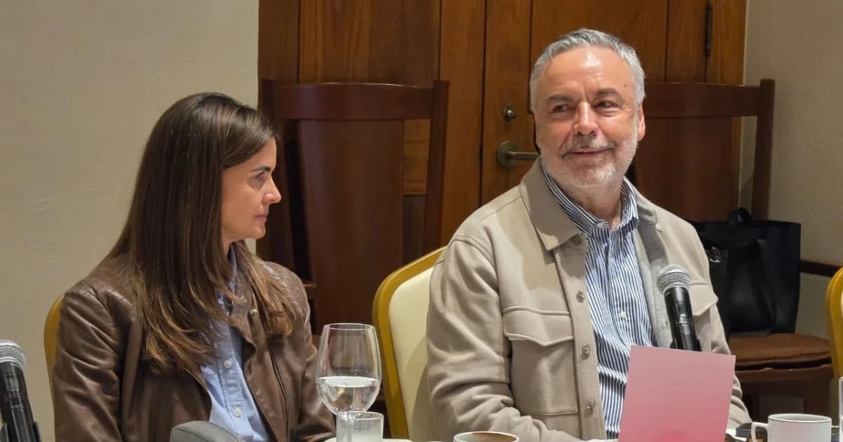 Dos participantes sentados en una reunión con micrófonos y documentos sobre la mesa.