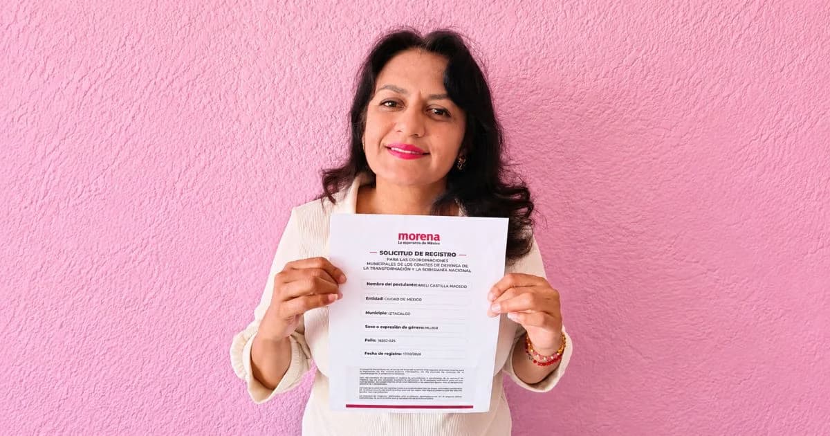 Mujer con blusa clara sostiene frente a una pared rosa una solicitud de registro con el logotipo de Morena.