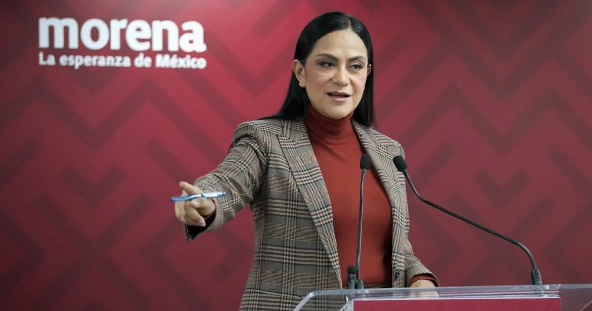 Ariadna Montiel habla ante micrófonos en un acto de Morena, con el emblema del partido sobre un fondo guinda