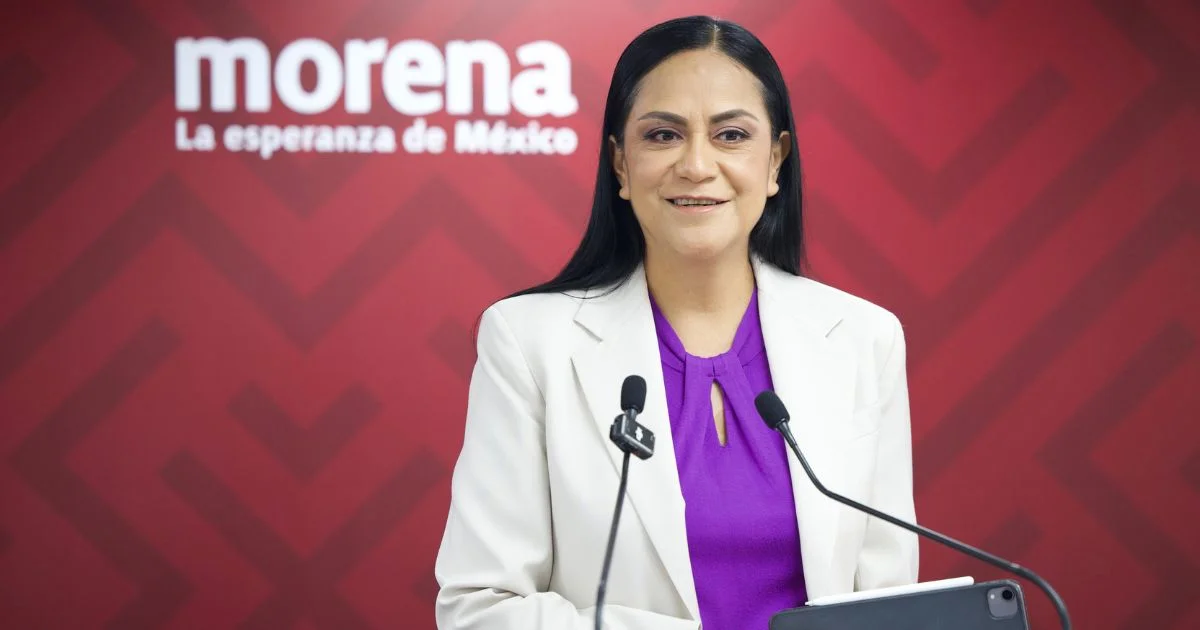 Mujer frente a dos micrófonos con el logotipo de Morena al fondo