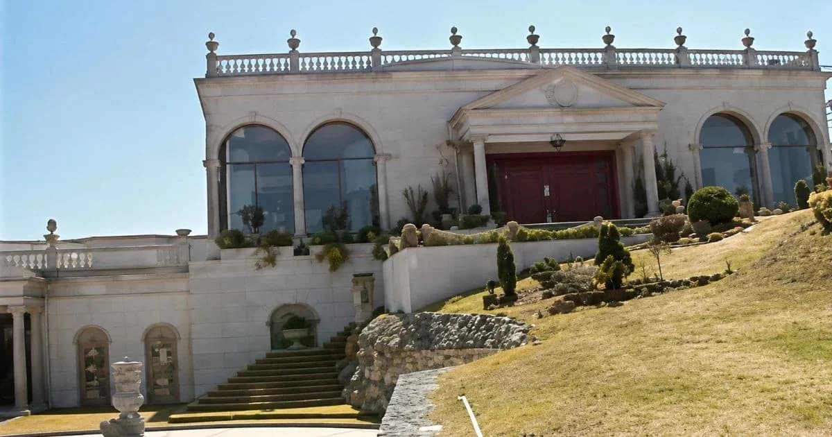 Fachada de una antigua residencia de piedra clara con escalinatas y puertas rojas