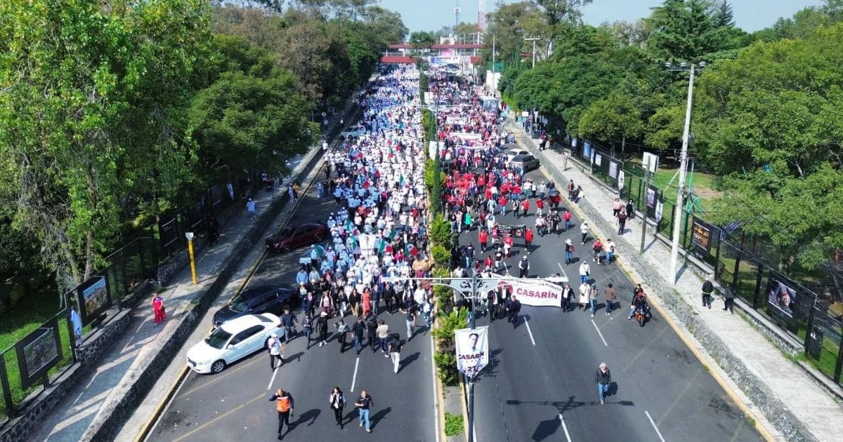 Vista aérea de una movilización de personas sobre una avenida arbolada, con una manta que menciona a Casarín