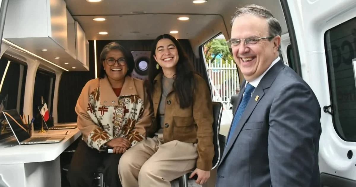 Tres personas posan junto a un vehículo acondicionado como espacio de trabajo, con una computadora portátil y una bandera de México
