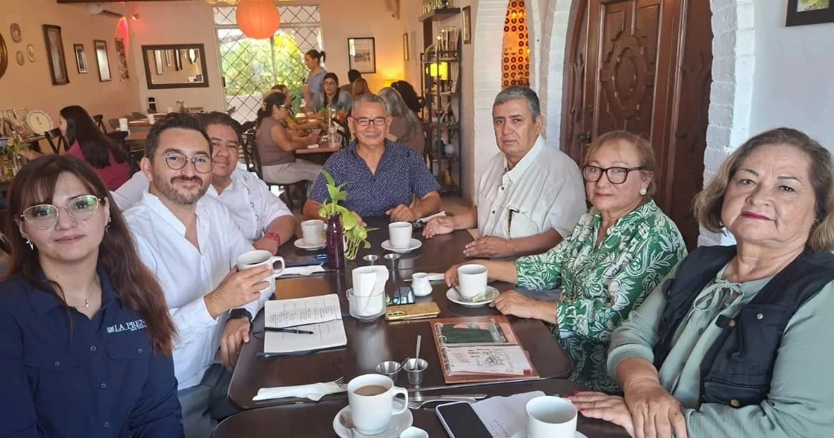 Grupo de siete personas sentado alrededor de una mesa en una cafetería, mirando a la cámara