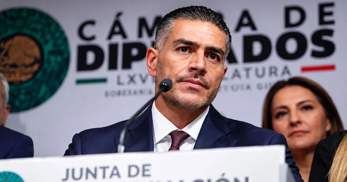 Un hombre de traje oscuro y corbata habla ante un micrófono durante un acto en la Cámara de Diputados; detrás aparecen otras personas y el emblema legislativo.