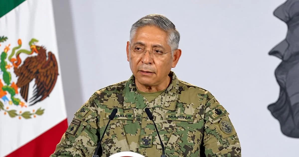 Almirante secretario de Marina en una intervención pública ante micrófonos y la bandera nacional.