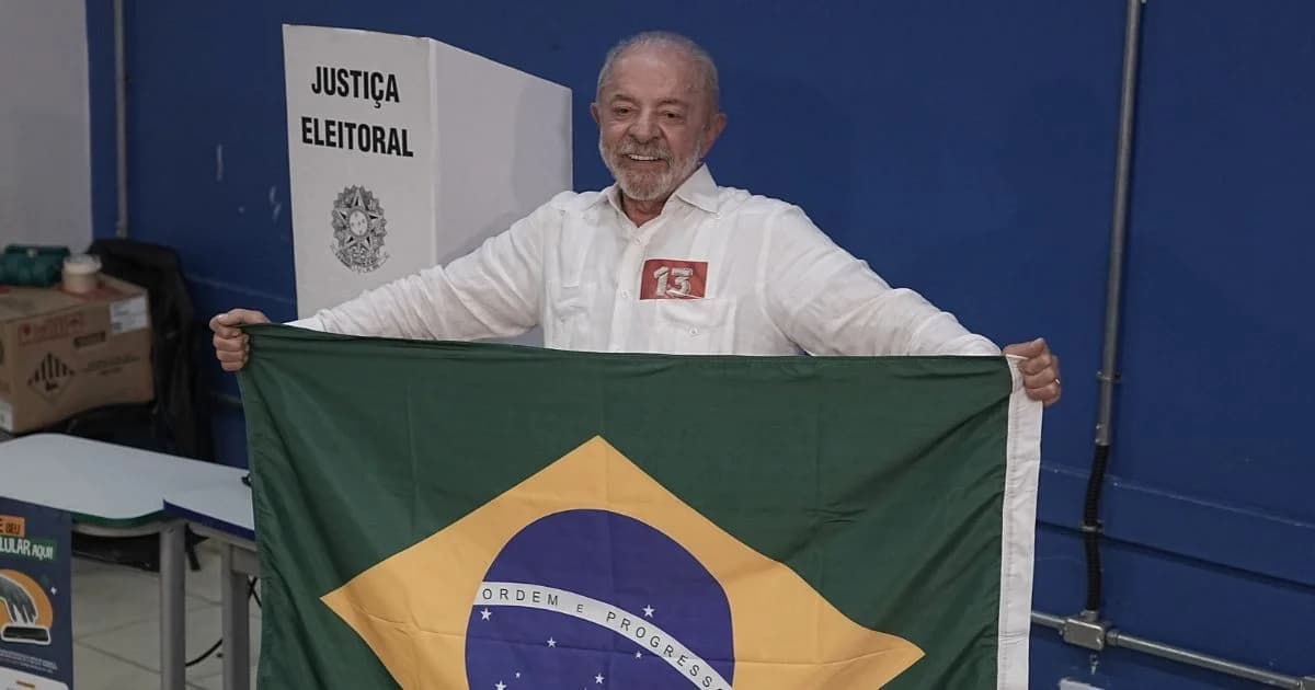 Luiz Inácio Lula da Silva sonríe mientras sostiene una bandera de Brasil frente a una mampara de justicia electoral
