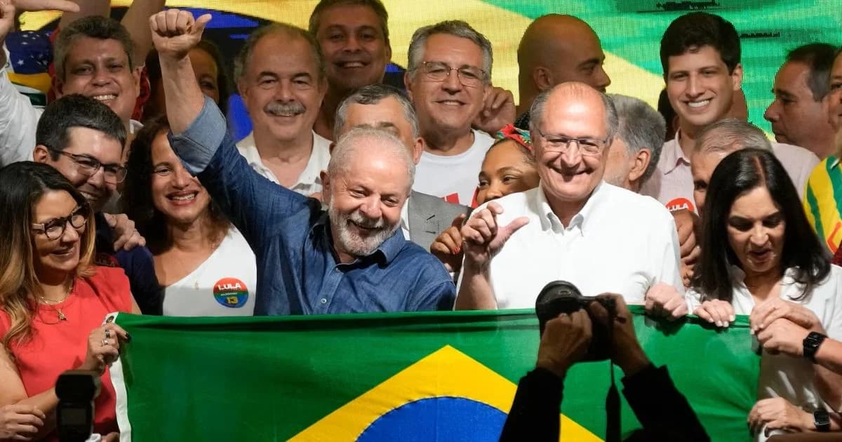 Lula da Silva levanta el brazo frente a seguidores con una bandera de Brasil en una celebración política.