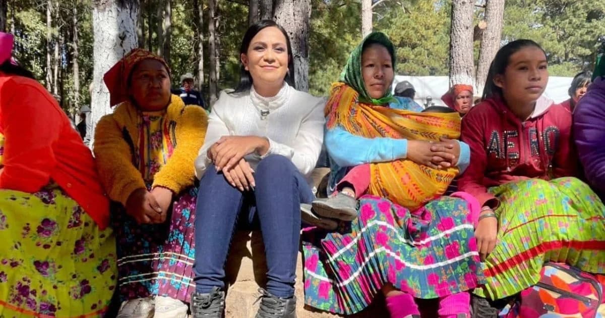 Ariadna Montiel sentada junto a mujeres en vestimenta tradicional en una zona arbolada