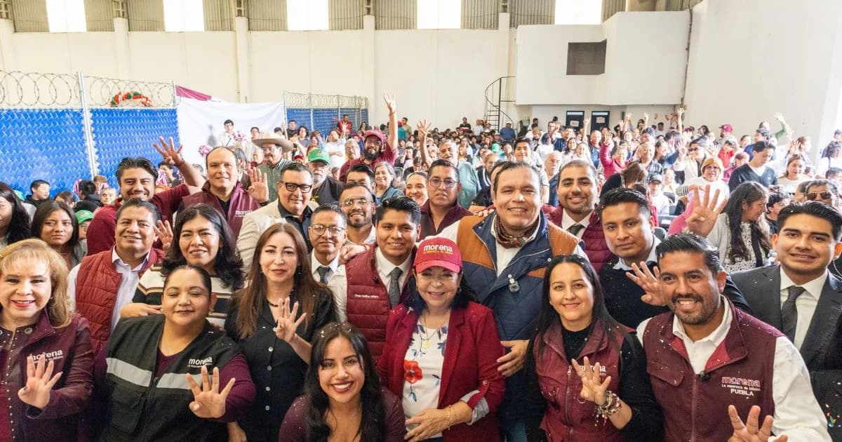 Grupo numeroso de personas posa en un recinto, varias con prendas de Morena y cuatro dedos levantados