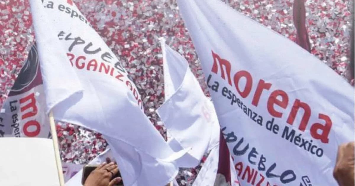 Banderas blancas con el nombre y emblema de Morena ondean frente a una multitud durante un acto político