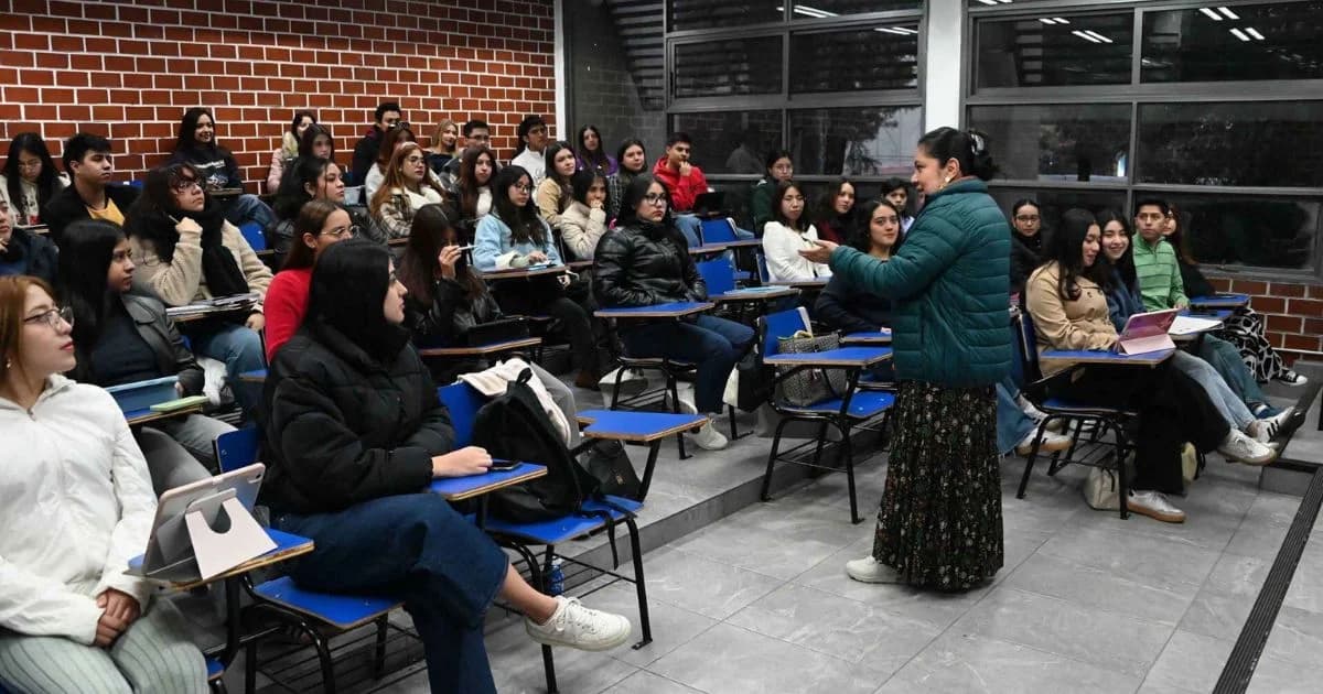 Grupo de estudiantes, en su mayoría mujeres jóvenes, escucha a una docente dentro de un aula