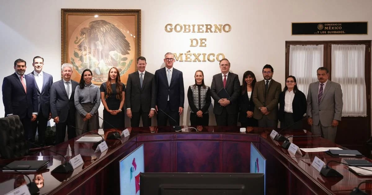 Grupo de personas posa en una sala de reuniones con el letrero Gobierno de México, una mesa de conferencias y un escudo nacional enmarcado.
