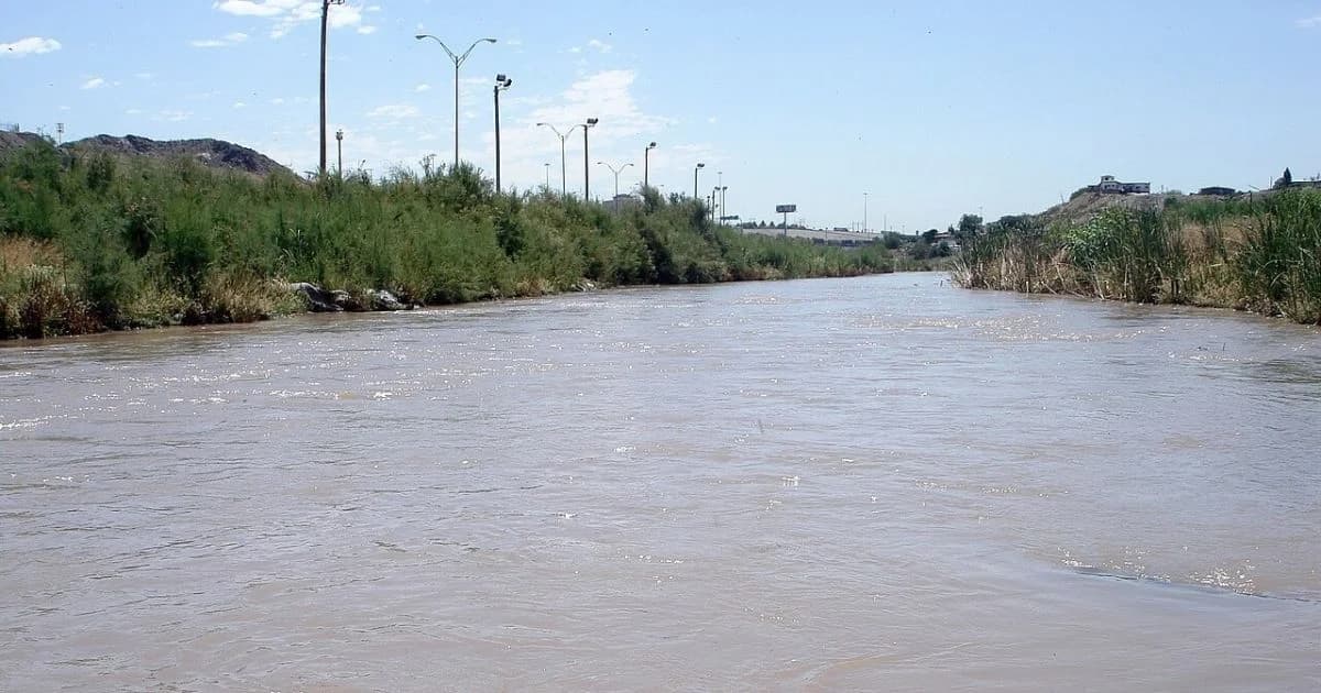 Vista del Río Bravo con aguas marrones, vegetación en ambas orillas y postes de alumbrado hacia el horizonte, entre Ciudad Juárez y El Paso.