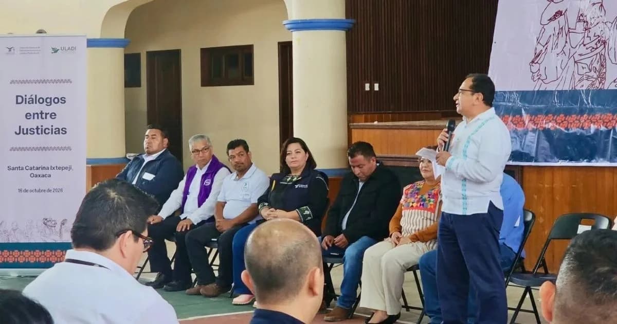 Ponente de pie con micrófono ante una mesa de participantes en el encuentro Diálogos entre Justicias en Santa Catarina Ixtepeji, Oaxaca