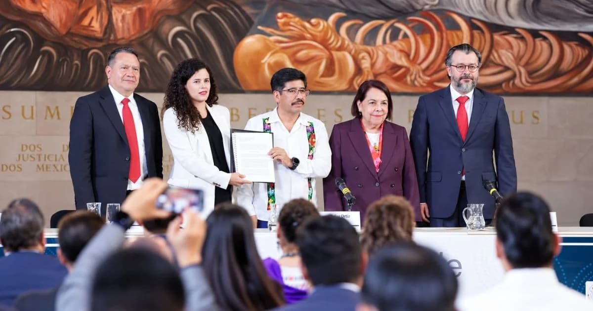Dos participantes en una conferencia institucional frente a micrófonos y documentos