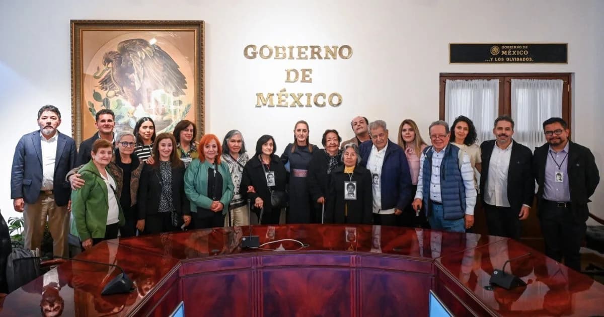 Grupo de personas posa en una sala oficial del Gobierno de México, algunas con fotografías colgadas al cuello