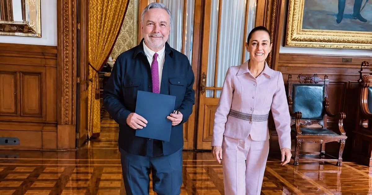 Dos personas caminan en un salón de Palacio Nacional; una de ellas sostiene una carpeta azul