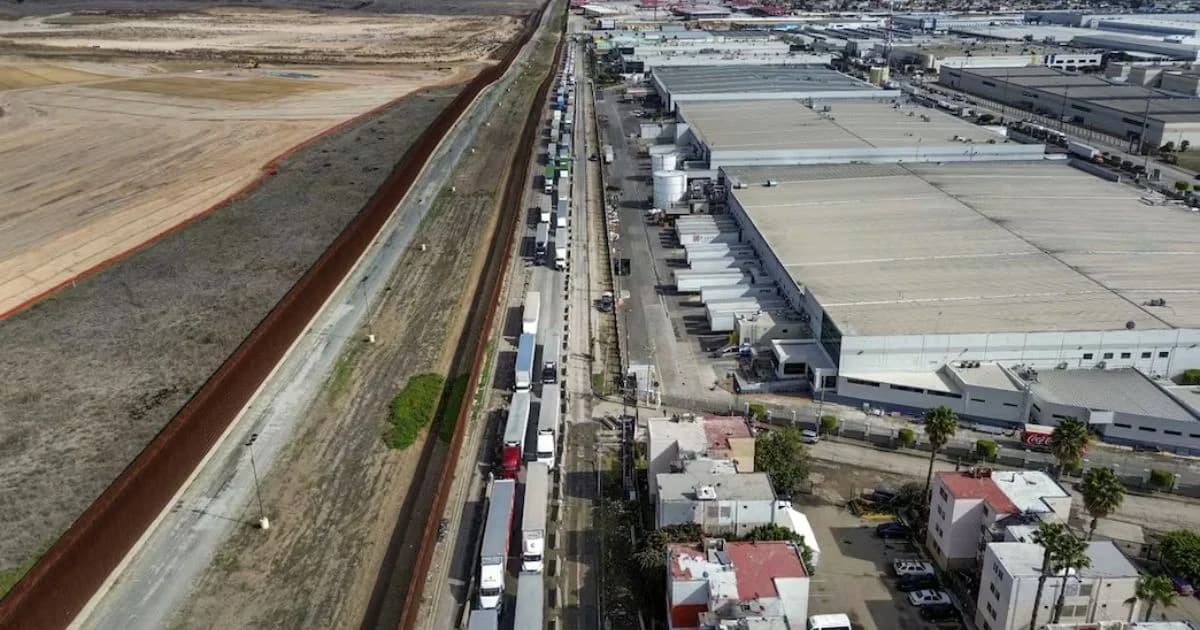 Fila de tractocamiones junto a una zona industrial en la frontera entre México y Estados Unidos ilustrando compras a EU
