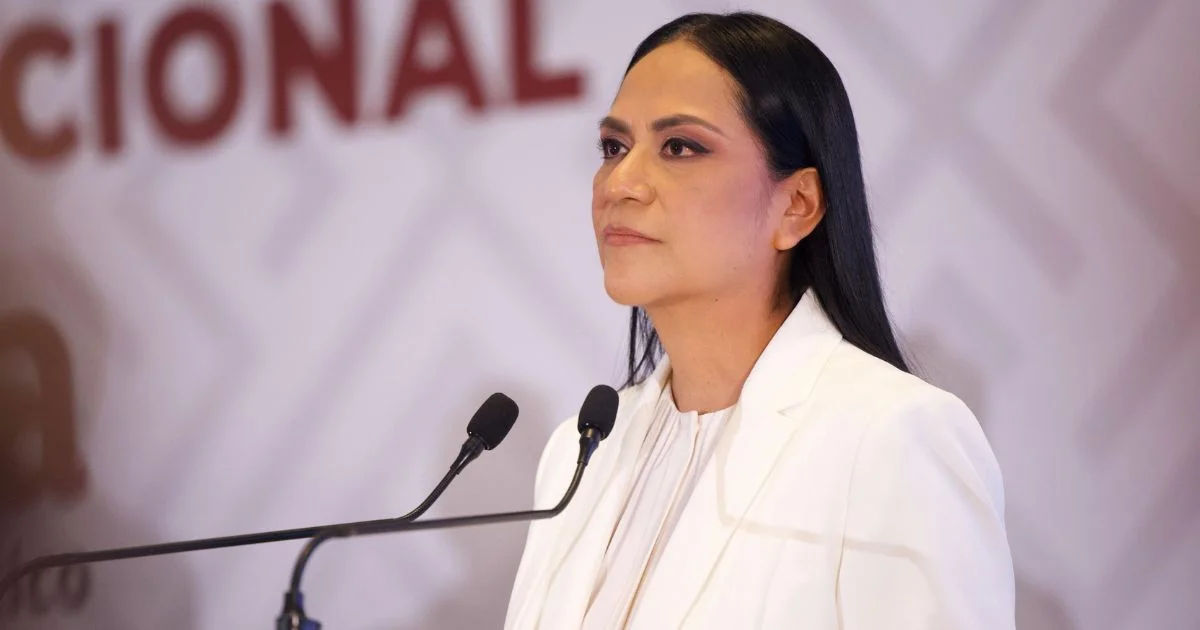 Mujer vestida de blanco frente a dos micrófonos durante un acto político