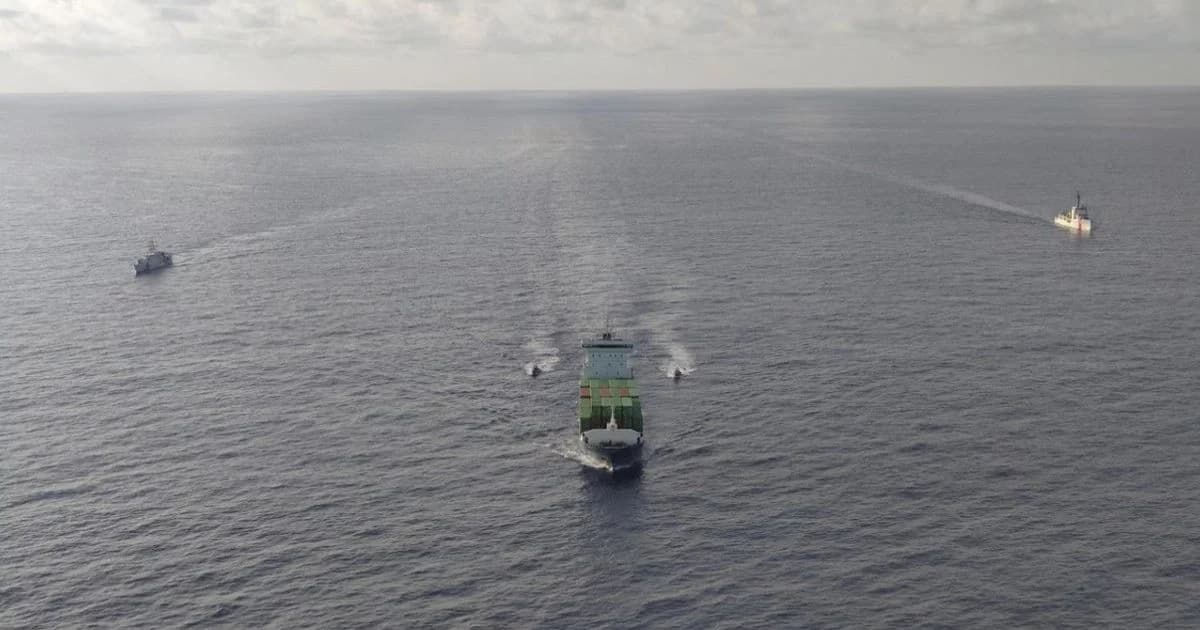 Un buque de carga navega en mar abierto acompañado a distancia por otras dos embarcaciones