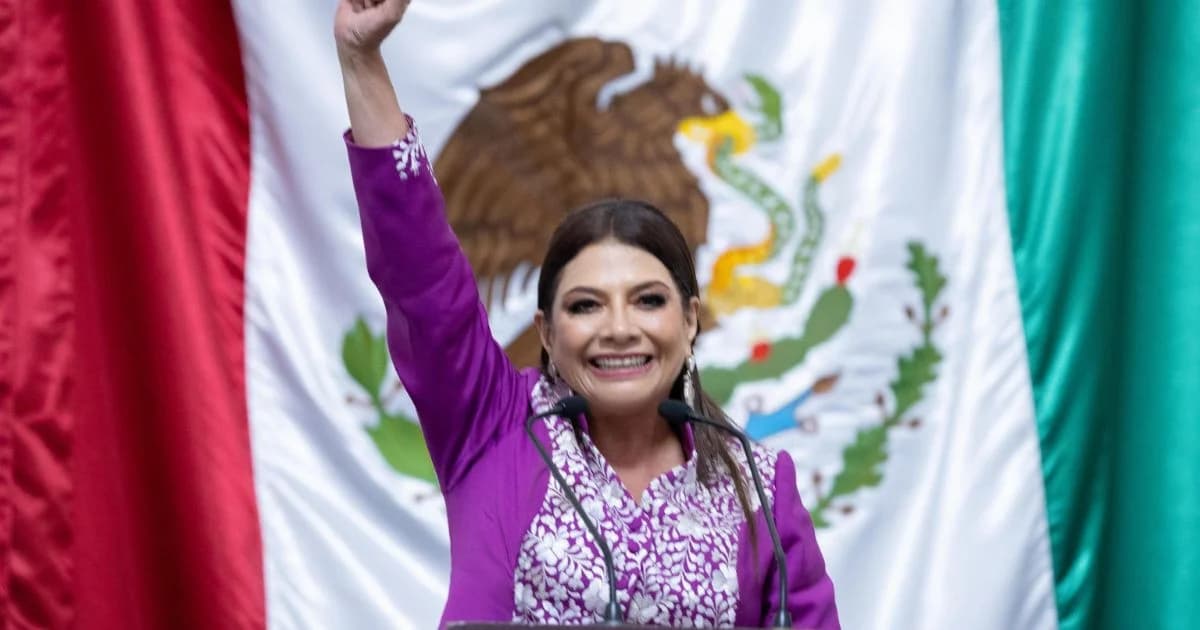 Clara Brugada con el puño en alto durante un acto ante la bandera de México