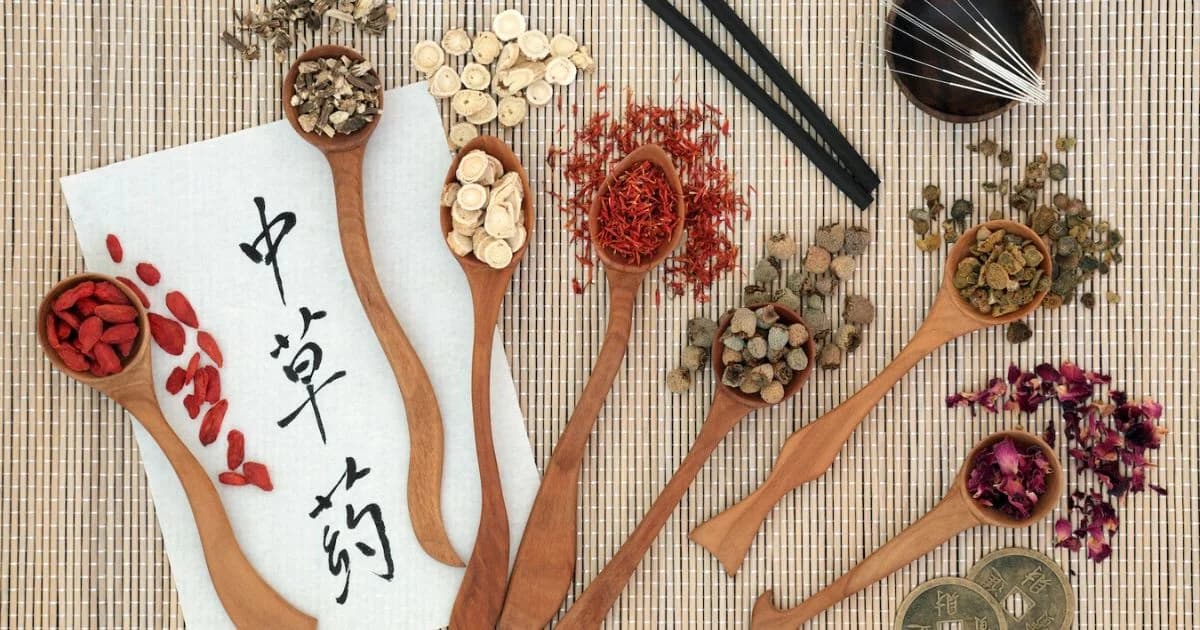 Cucharas de madera con plantas secas, raíces, bayas y flores sobre una esterilla de bambú junto a caracteres chinos