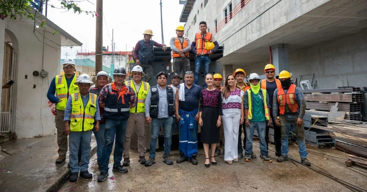 Trabajadores de la construcción con chalecos y cascos posan junto a autoridades frente a un edificio hospitalario en obra