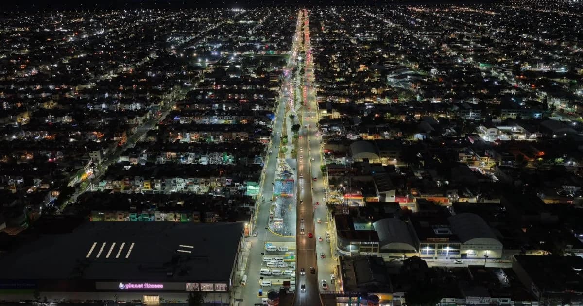 Vista aérea nocturna de una avenida iluminada y las colonias a su alrededor.