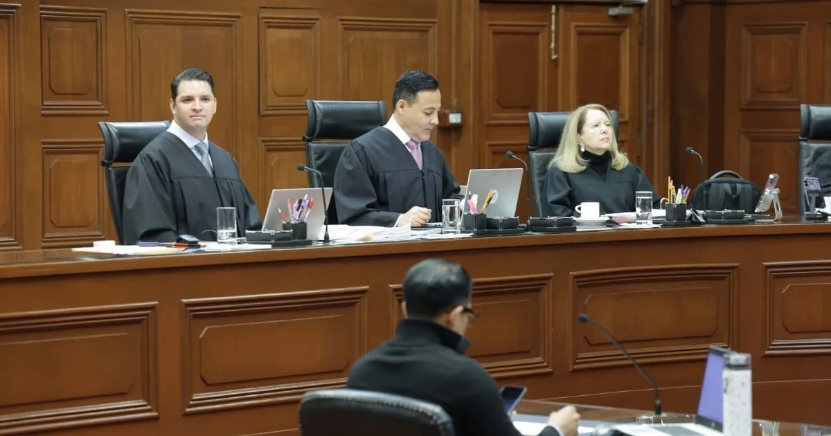 Tres integrantes de un tribunal con toga negra participan en una sesión dentro de una sala con paneles de madera.